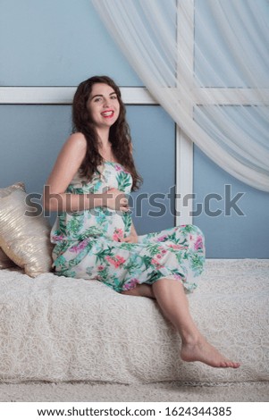 Beautiful young pregnant woman with curly hair in a long dress, Studio shooting