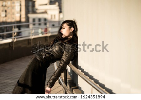 Girl in black with black aggressive make up with skull-like bag is standing behind white wall in a city. Might be a picture representing subculture, youth, teenagers
