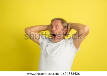Astonished, shocked, wondered. Caucasian man portrait isolated on yellow studio background. Beautiful male model in white shirt posing. Concept of human emotions, facial expression, sales, ad, bet.