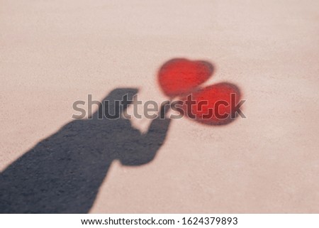 Romance and loneliness in city: shadow of person (man or woman) holding two heart-shaped balloons. Silhouette on grey tarmac with red hearts above. Looking for love concept, Room for copy text