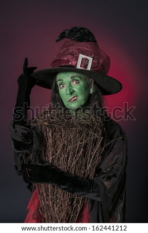 Halloween witch with green face and broomstick on red background