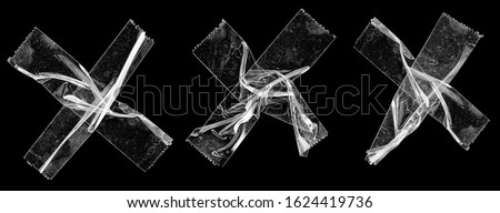 three sets of transparent sticky tapes forming the letter x or overlapping each other on black background, crumpled plastic snips, poster design overlays or elements. Royalty-Free Stock Photo #1624419736