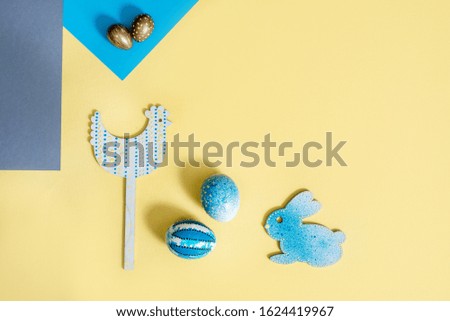 Wooden chicken, easter blue bunny and eggs on a paper background.Easter table, place setting. Easter egg, blue color painted, and grey napkin, yellow background, top view.