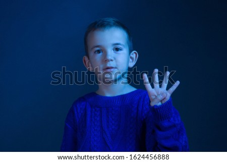 Studio portrait of a brunette Boy who counts on his fingers, shows four finger