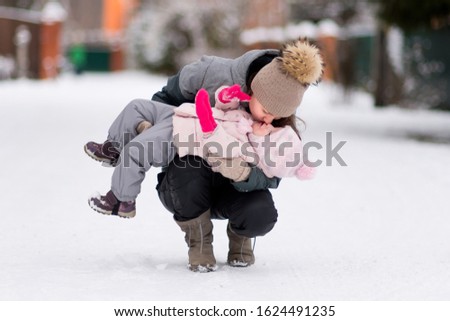A young mother holds a little daughter in her arms and kisses her on a snowy winter morning. Winter family walks