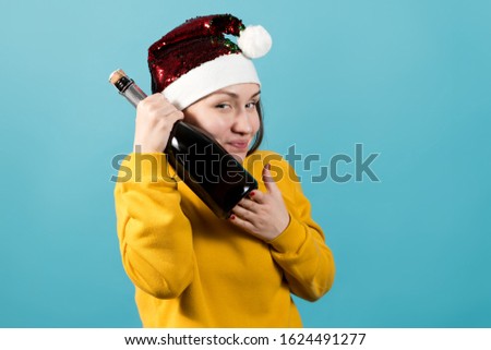 A girl in a Christmas hat with a sly smile clings to a bottle of champagne in anticipation of the holiday