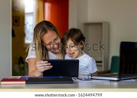 Happy mom and cute little son having fun,learning using mobile.Mother watching son playing games on tablet.Son and his mother using online media laptop,smartphone and digital tablet.Mobile addiction.
