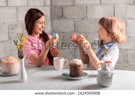 Happy little girl and boy playing traditional Easter game - egg tapping with colored eggs at home