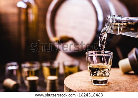 Glass of golden rum, with bottle. Bottle pouring alcohol into a small glass. Brazilian export type drink. Brazilian product for export, distilled drink known as brandy or pinga. Day of cachaça. Royalty-Free Stock Photo #1624518463