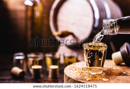 Glass of golden rum, with bottle. Bottle pouring alcohol into a small glass. Brazilian export type drink. Brazilian product for export, distilled drink known as brandy or pinga. Day of cachaça. Royalty-Free Stock Photo #1624518475