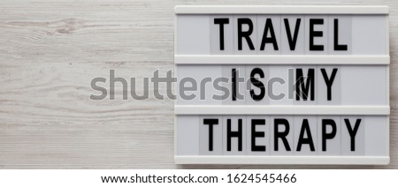 'Travel is my therapy' words on a modern board on a white wooden background, top view. Overhead, from above, flat lay. Copy space.