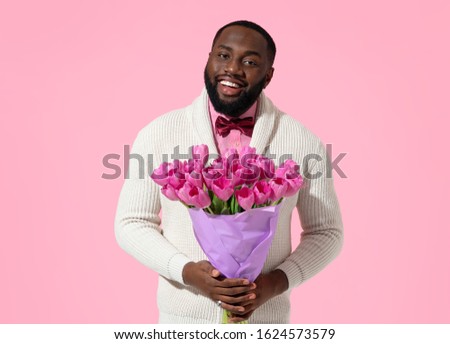 Handsome man holds bouquet of spring flowers. Photo of african american man expresses love to someone, romantic feelings on pink background