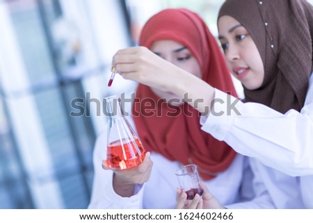 Two female Muslim scientists wear a white coat and look at a glass test tube during an experiment in a chemical laboratory.