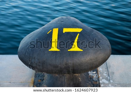 Number 17, seventeen, stencil yellow digit painted on a big commercial harbor bollard. Royalty-Free Stock Photo #1624607923