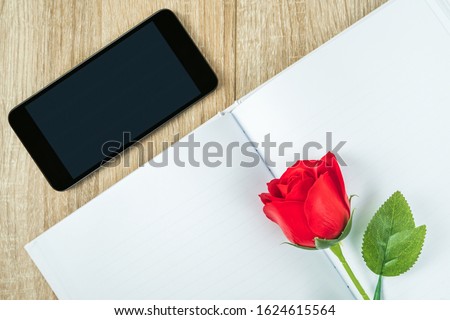 Top view shot of red roses on blank notebook diary and  smartphone on wood table,Valentine concept