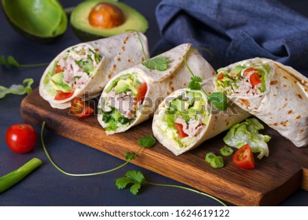 Turkey wraps with avocado, tomatoes and iceberg lettuce on chopping board. Tortilla, burritos, sandwiches, twisted rolls