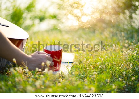 Women hold cup of coffee and coffee on a book in the park;
