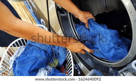 The hands of people are putting clothes into the washing machine for cleaning. Is a modern washing machine preserving fabric.