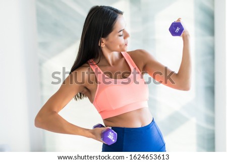 Sporty beautiful woman exercising with dumbbell at home to stay fit