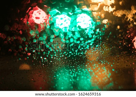 Colorful raindrops on windshield at night with blurred traffic lights
