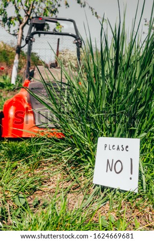 close up view of electric lawn mower cutting a bush with a sign please no