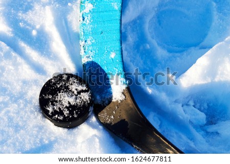 Composite hockey stick and puck are lying on the snow during a yard match. Winter sports in the backyard