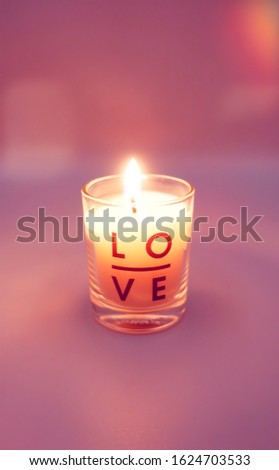 Close up of burning candle with love print on glass on pink background with beautiful bokeh for valentine's day and anniversary, love, greeting, proposal, wedding card concept with copy space