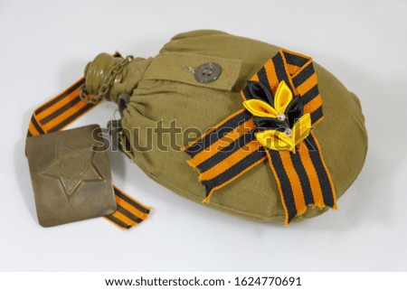 St. George ribbon lying on a soldier’s flask and a metal buckle of an old Soviet soldier’s belt, isolate on a white background