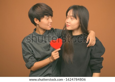 Young Asian lesbian couple together and in love against brown background