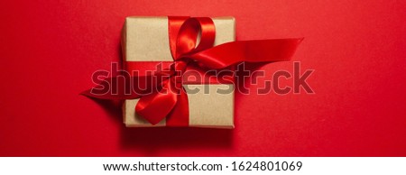 Brown paper gift box with a red satin ribbon bow on red background. Flat lay top view above. Holidays, Valentines day and gifts concept