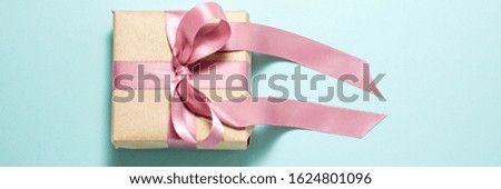 Banner of brown paper gift box with a purple satin ribbon bow on blue background. Flat lay top view. Gift andholidays concept from above with copy space