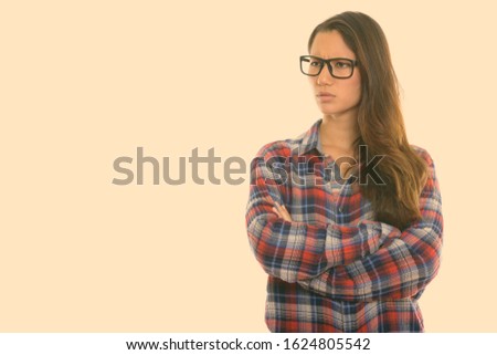 Studio shot of young angry woman thinking with arms crossed while wearing eyeglasses