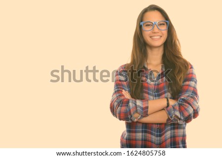 Studio shot of young happy woman smiling while wearing eyeglasses with arms crossed