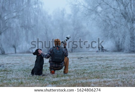 Photographer man and his dog looking something in the winter park