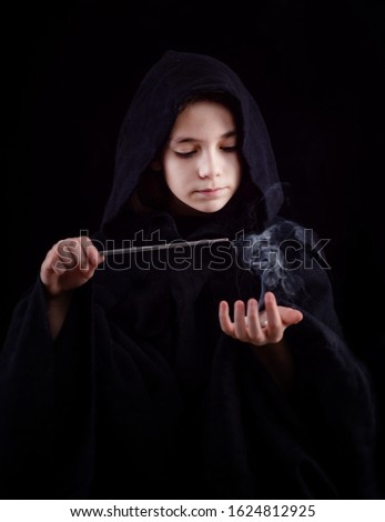 A girl in a witch's cloak with a magic wand in his hand conjures magic. Halloween outfit