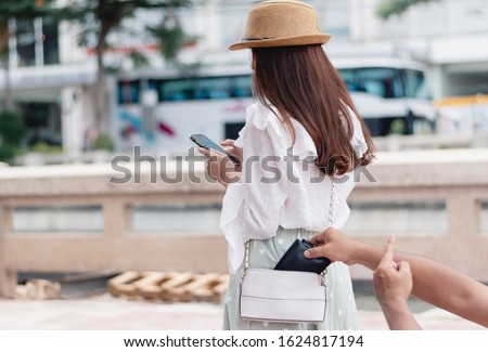 Stealing wallet from the pickpocket from shoulder bag of tourist girl, The use of mobile phones makes them unattended and makes them a target for thieves. Royalty-Free Stock Photo #1624817194