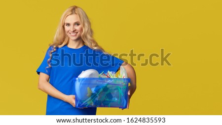 Caring for nature. Young woman in a blue T-shirt are holding a box with plastic bottles and waste. Volunteer compiled garbage and carry it to recycling. Yellow background