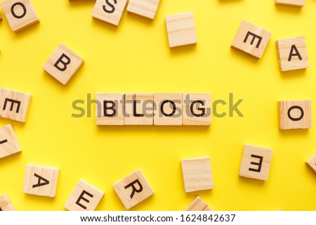 Wooden cubes letters with the word blog on a yellow background. Top view, flat lay.