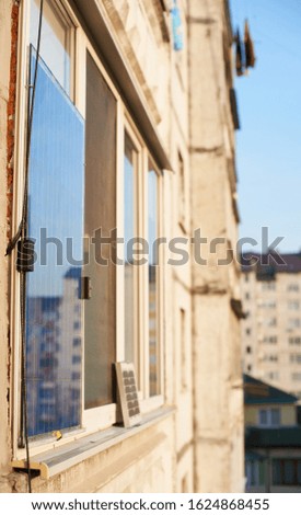 Solar battery on the window of a high-rise residential building against a background of a sleeping area of the city with clear blue sky on a warm day. Converting solar radiation into electricity