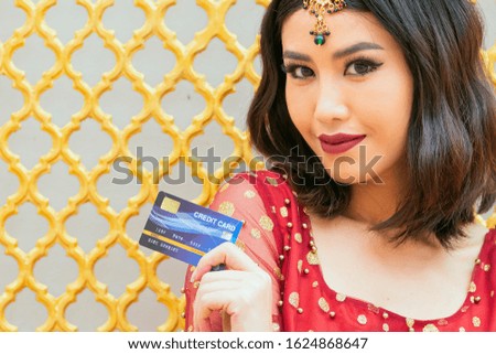 Young smiling beautiful Asian woman wearing Traditional India costume presenting credit card in hand showing trust and confidence for making payment. Copy space