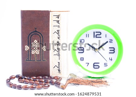 A picture of Al Quran with clock and prayer beads for read Koran concept. The Arabic translation is "the verse in Quran is original and never been authored". 