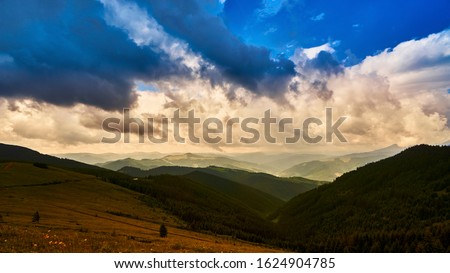 Majestic sunset and beautiful landscape in the mountains. Flooding fog between the peaks. Fragment of a blue sky with clouds. Summer beautiful sunny evening. Moving and red sun colorful sky background