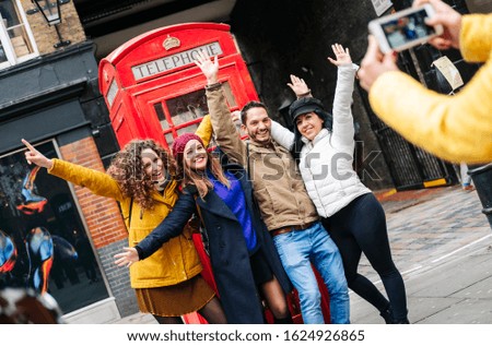 A group of friends take a picture in a London street with a red telephone booth while they laugh and are happy