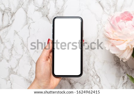 Mobile phone in in female hand with piony flowers on a marble background, using technology concept for the holidays - Valentine's Day, Women's and Mother's Day. Floristics and decoration