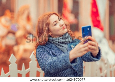Young beautiful girl takes a selfie on her phone on the street. Take a picture.