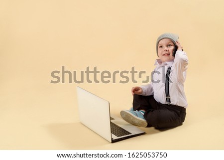 Cute little blonde boy works at a computer. holding a gold bank card. The concept of business, online work, work on the Internet. Working at a laptop