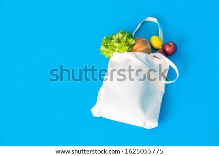 Cotton eco-bag with green fresh kale and fruits on the blue background.