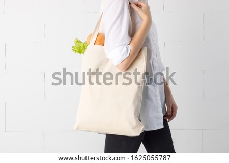 Girl is holding cotton eco-bag with green fresh kale and bread.
