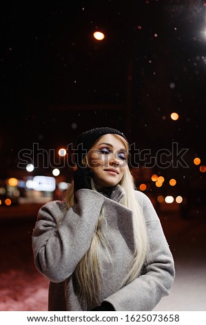 Beautiful blonde in a hat in the evening on the street. Winter portrait of a girl with makeup