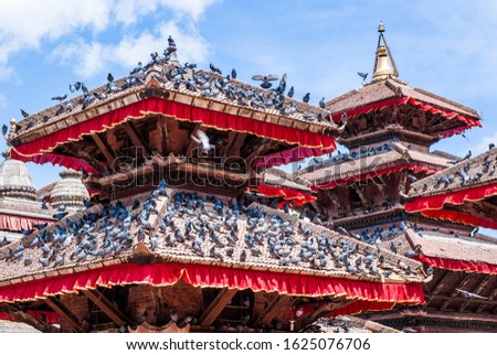 Picture of an ancient building with many pigeons on the roofs at sunny day with cloudy blue sky on background. Famous place Durbar Square in Kathmandu, capital of Nepal. UNESCO World Heritage Site.